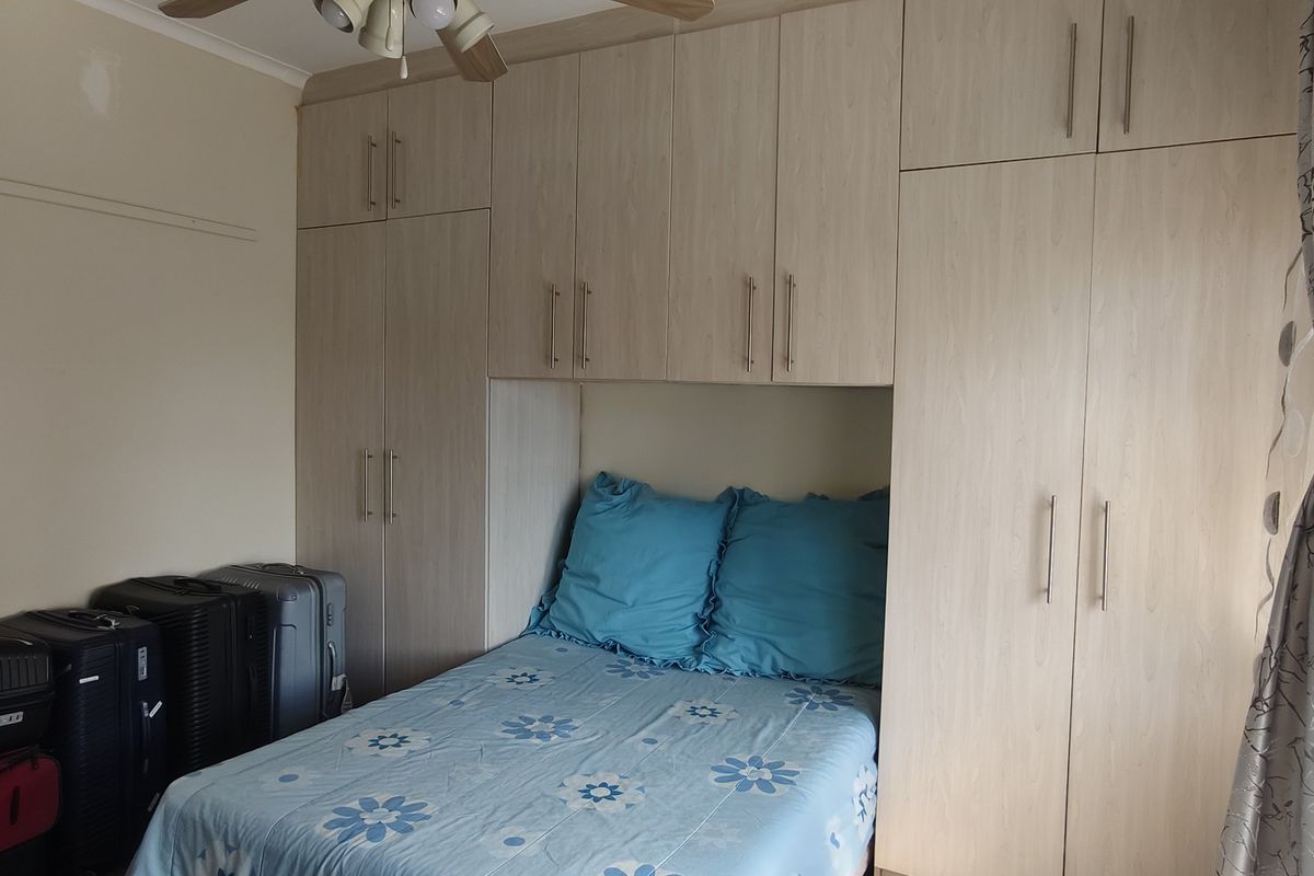 A bedroom featuring extensive light wood-finish built-in cupboards providing ample storage space and a ceiling fan.