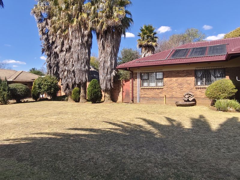 Spacious rear garden featuring a brick-faced house with a tiled roof, solar water heating panels, and secure metal fencing.