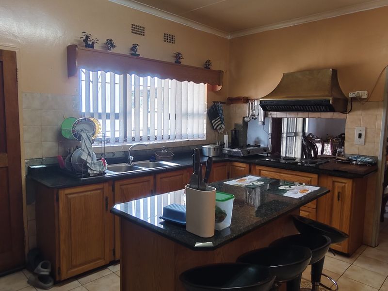 A functional kitchen featuring wooden cabinetry, granite countertops, a central island, and an integrated extractor fan, with direct access to an adjacent dining area.