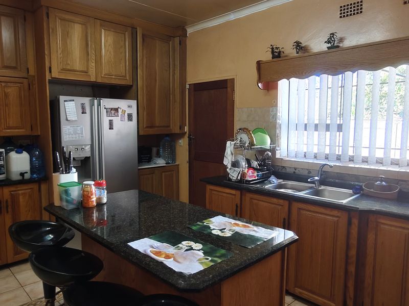 A traditional kitchen featuring wooden cabinetry, granite countertops, a central island, and a double basin sink with natural light from the window.