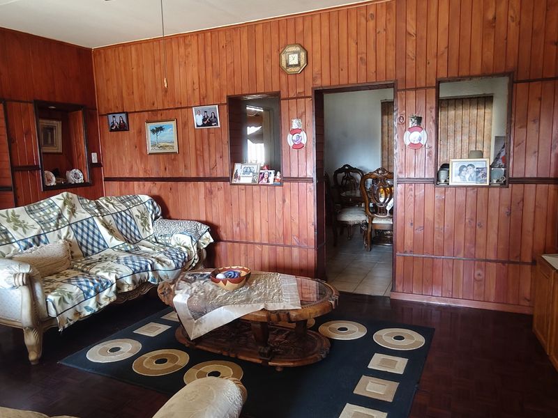 A living room featuring traditional timber wall paneling and parquet flooring, with an open archway leading to an adjacent dining area.