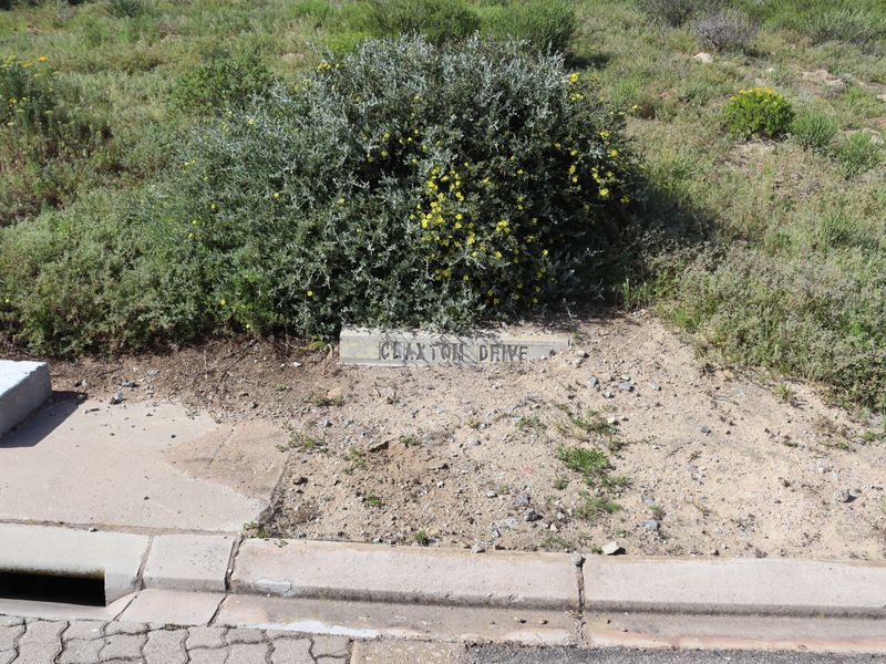 A street-level view showing the concrete curb, stormwater drainage, and street name marker for Claxton Drive on the vacant residential land.