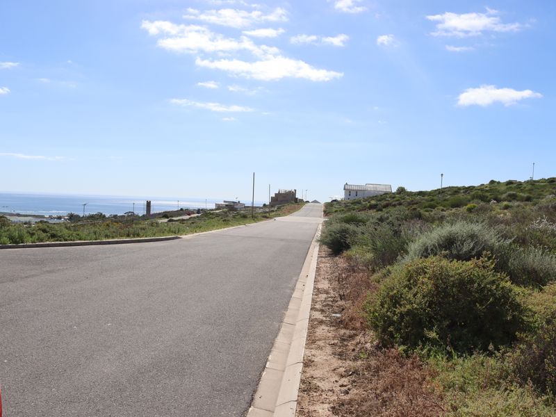 A view of the paved street leading through the residential area, featuring coastal surroundings and clear sky.