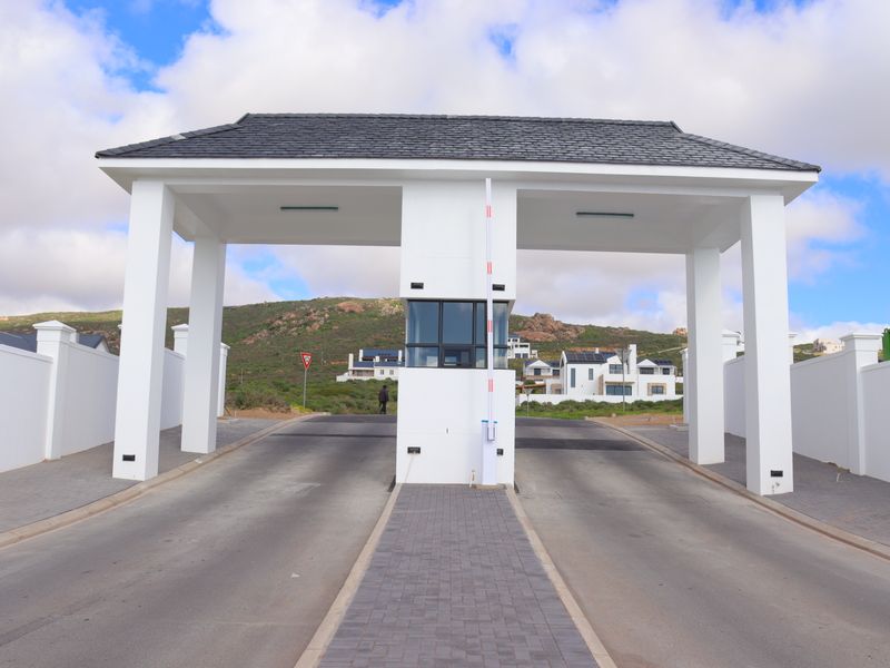 A modern, well-maintained security gatehouse entrance featuring a boom gate, paved driveway, and clean architectural lines at the estate access point.