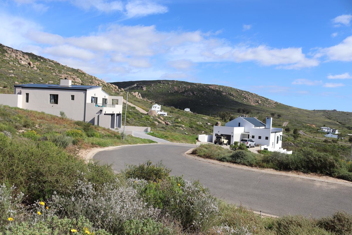 A street-level view of a residential area featuring modern homes set against a scenic, hilly landscape with natural vegetation.
