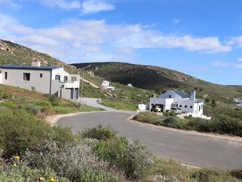 A street-level view of a residential area featuring modern homes set against a scenic, hilly landscape with natural vegetation.