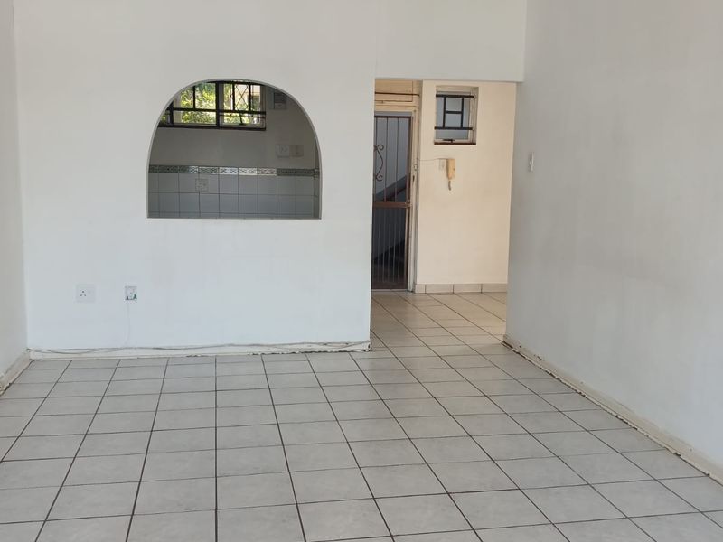 An empty living area featuring tiled flooring, a ceiling fan, and an arched serving hatch connecting to the kitchen area.