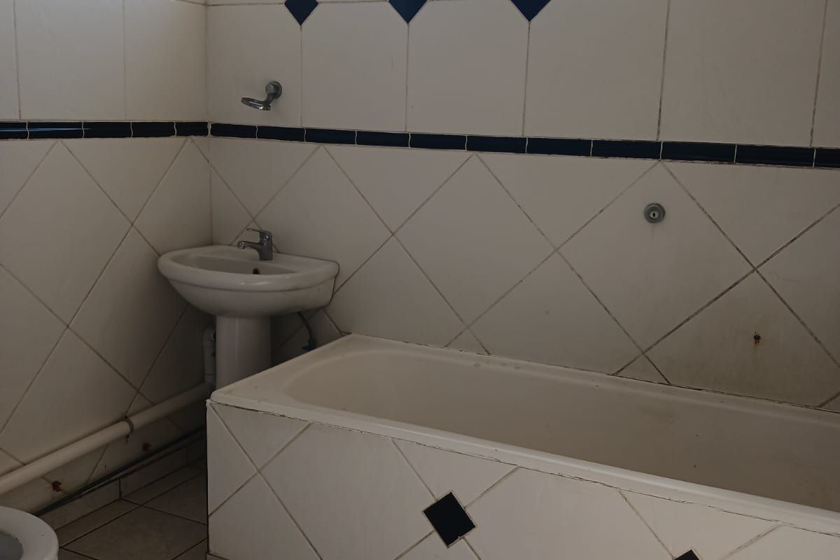A dated bathroom featuring a tiled bathtub, pedestal basin, and toilet with classic ceramic wall and floor tiling.