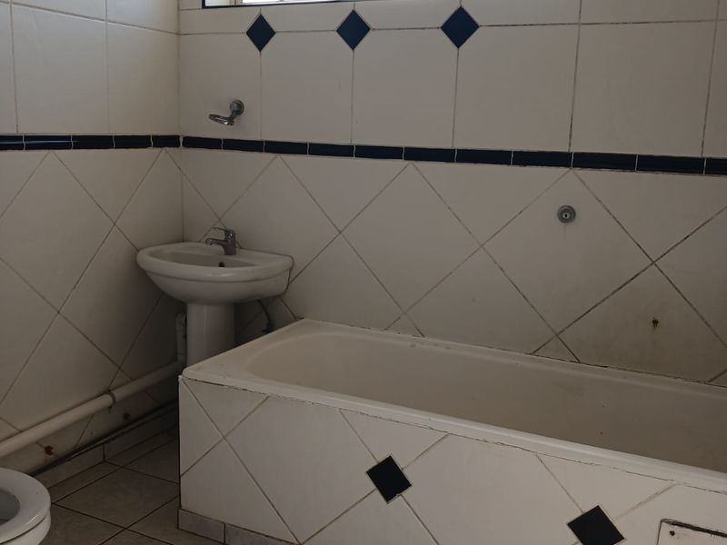 A dated bathroom featuring a tiled bathtub, pedestal basin, and toilet with classic ceramic wall and floor tiling.