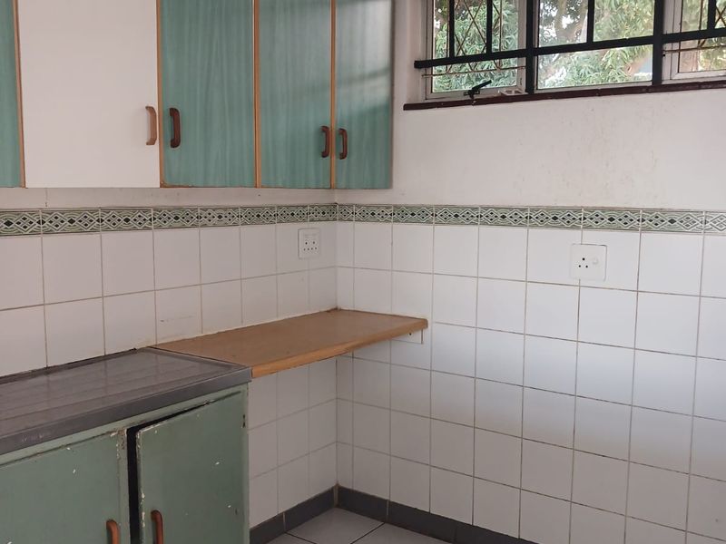 A functional kitchen space featuring built-in cabinetry, tiled splashbacks, and tiled flooring, ready for a modern renovation to update the dated finishes.