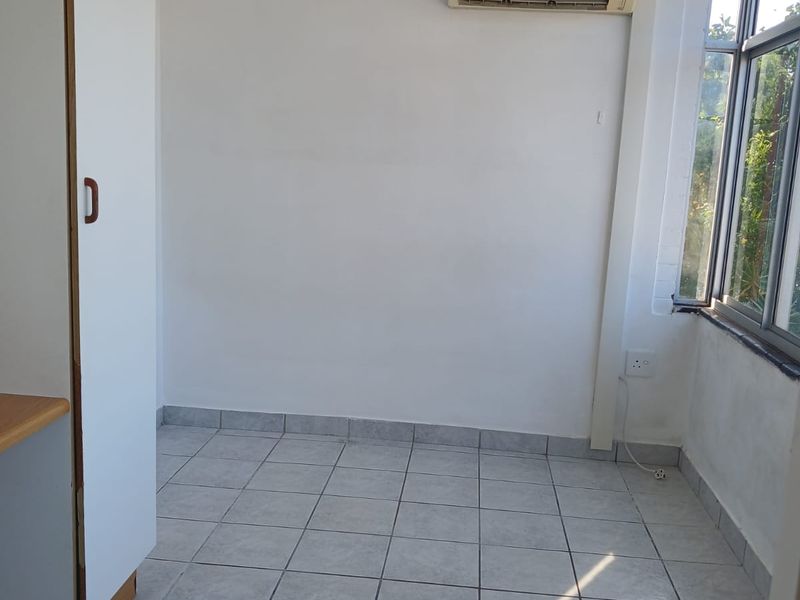 An empty bedroom featuring tiled flooring, a built-in wardrobe, and a wall-mounted air conditioning unit.