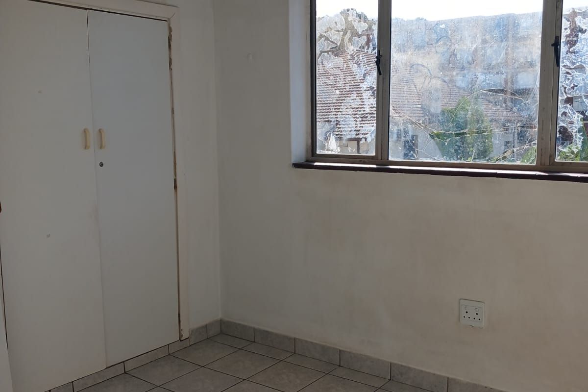 An empty bedroom featuring tiled flooring, a built-in wardrobe, and a window with visible glass damage.