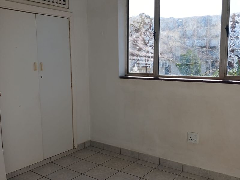 An empty bedroom featuring tiled flooring, a built-in wardrobe, and a window with visible glass damage.