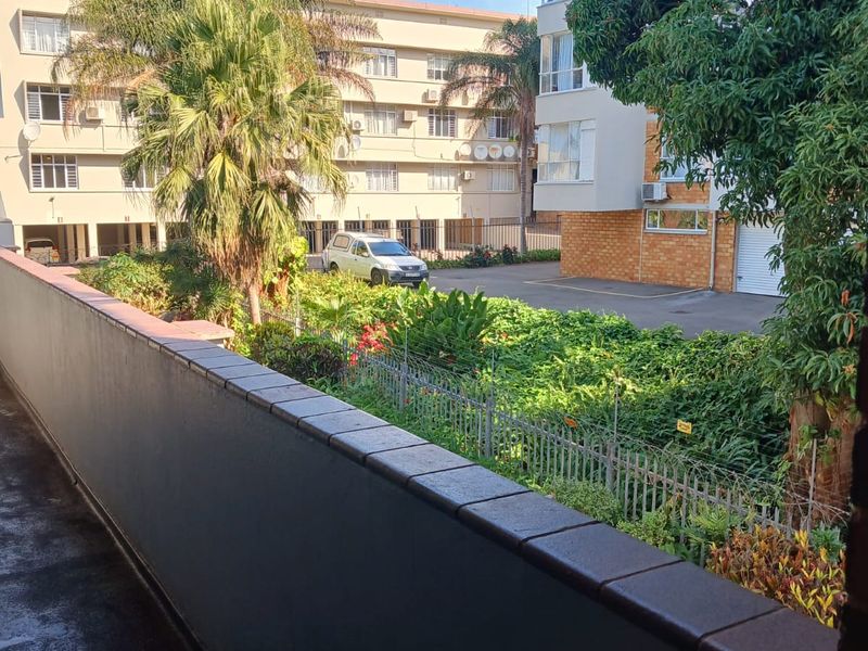 A view from a balcony overlooking a landscaped garden area and adjacent apartment building complex.