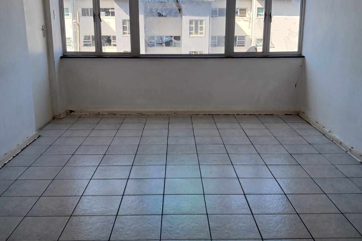 An empty, sunlit living area featuring neutral tiled flooring and a large window assembly, providing a blank canvas for interior design.