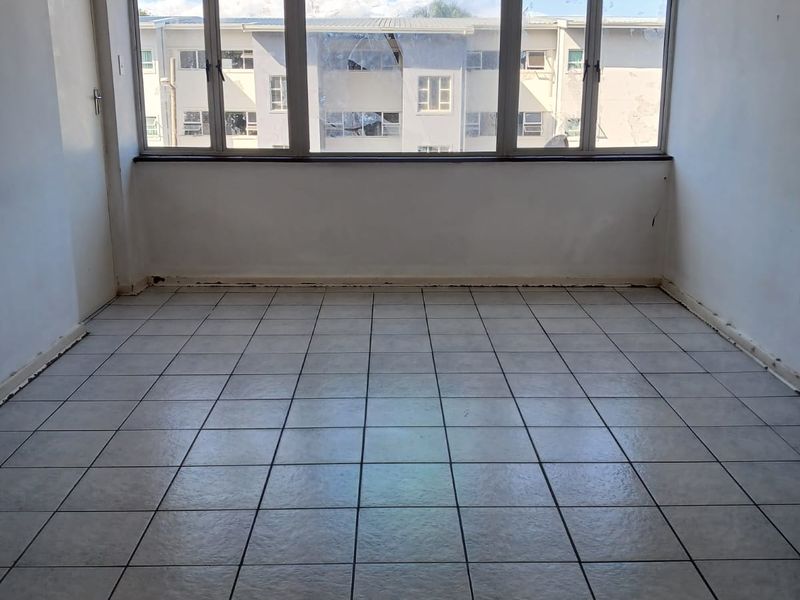 An empty, sunlit living area featuring neutral tiled flooring and a large window assembly, providing a blank canvas for interior design.