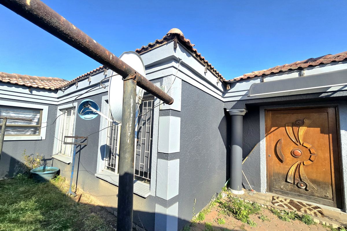 Front entrance view of the house featuring a decorative wooden door, tiled roof, and security bars on the windows.