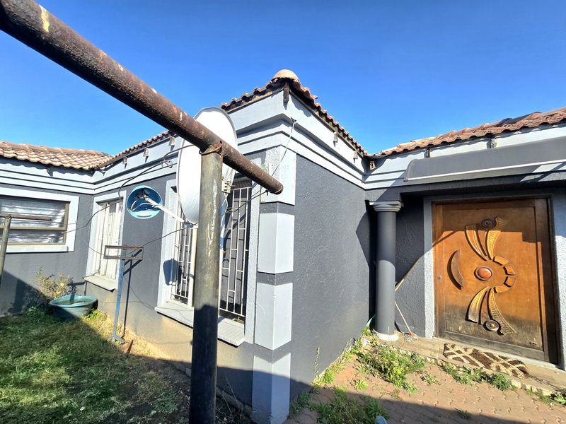 Front entrance view of the house featuring a decorative wooden door, tiled roof, and security bars on the windows.