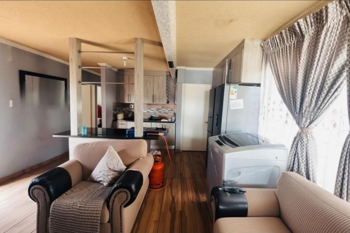 Open-plan living and kitchen area featuring laminate flooring, built-in cabinetry, and a breakfast bar, offering a functional layout for daily living.