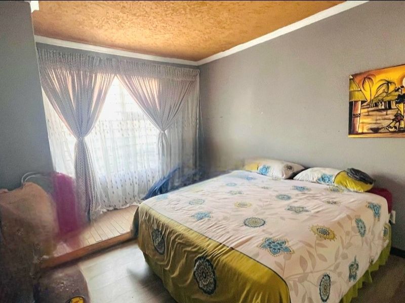 A bedroom featuring laminate flooring and a textured ceiling, offering a functional space with natural light from the window.