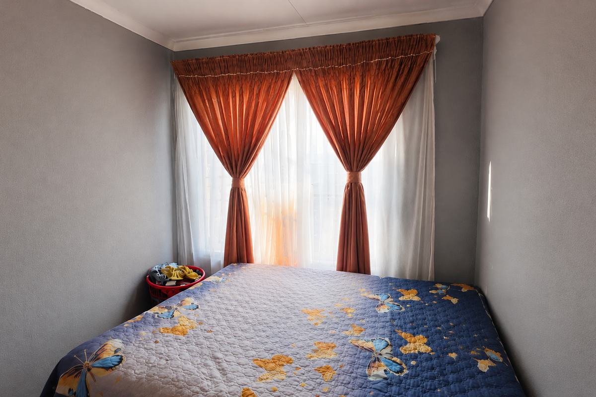 A standard bedroom featuring neutral grey walls, coving, and a window dressed with layered curtains.