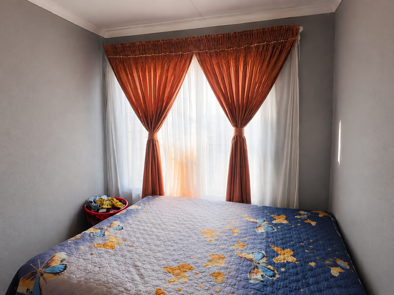 A standard bedroom featuring neutral grey walls, coving, and a window dressed with layered curtains.