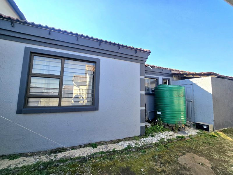 Rear exterior view of the property featuring a water storage tank, plastered walls, and aluminium window frames with security bars.