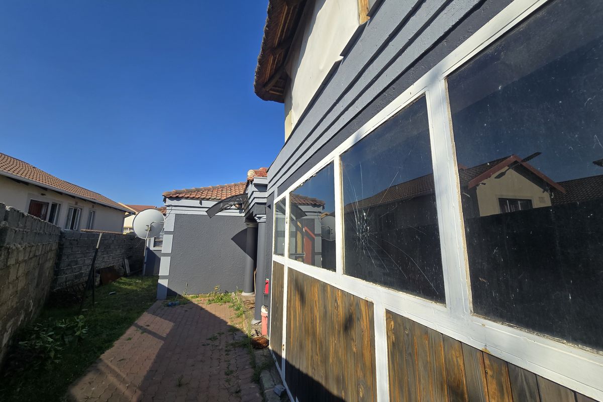 Rear exterior view of the property featuring a paved walkway, boundary wall, and a section of the building with a cracked window pane.