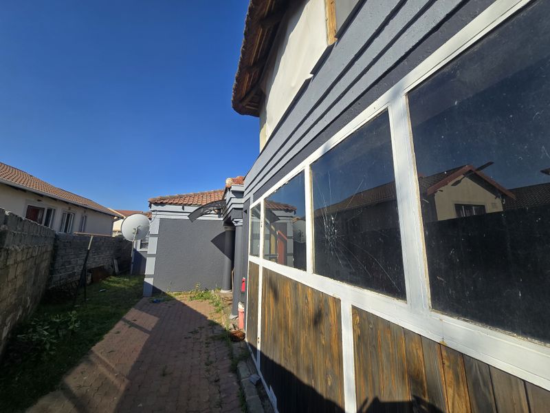 Rear exterior view of the property featuring a paved walkway, boundary wall, and a section of the building with a cracked window pane.