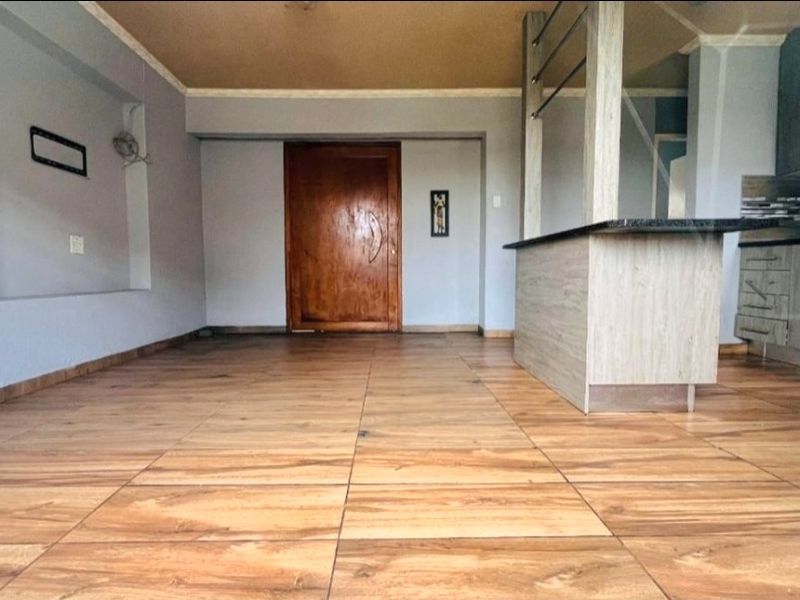 Open plan living and kitchen area featuring wood-look tiled flooring, a breakfast bar with granite countertop, and built-in kitchen cabinetry.