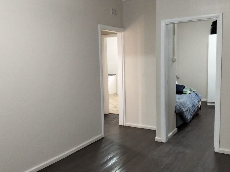 A neutral hallway with dark laminate flooring providing access to adjacent rooms, including a bedroom and kitchen area.
