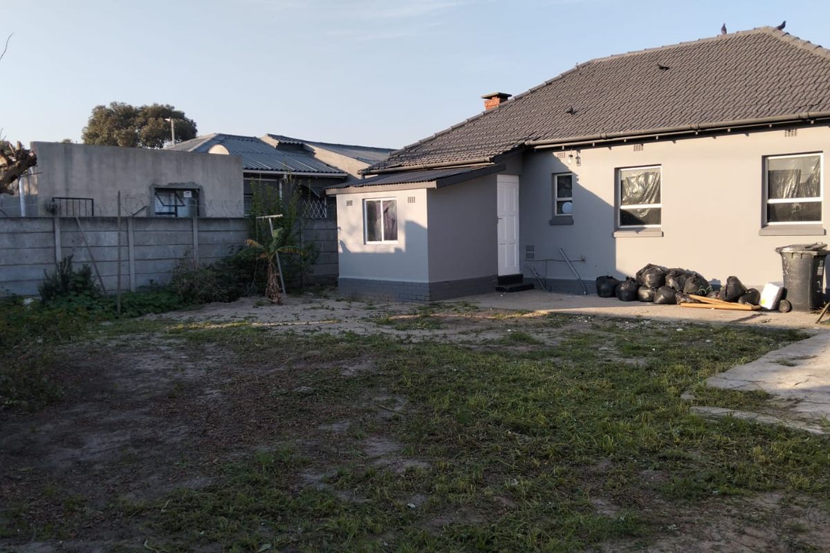Rear view of the house showing a paved patio area, tiled roof, and a large backyard with a concrete boundary wall.