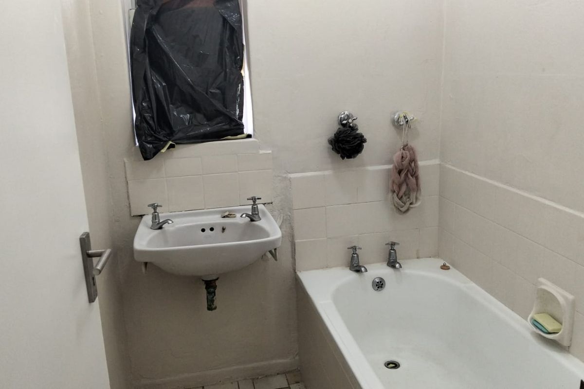 A compact bathroom featuring a wall-mounted basin and a built-in bathtub with tiled splashbacks, requiring cosmetic updates to improve its overall condition.