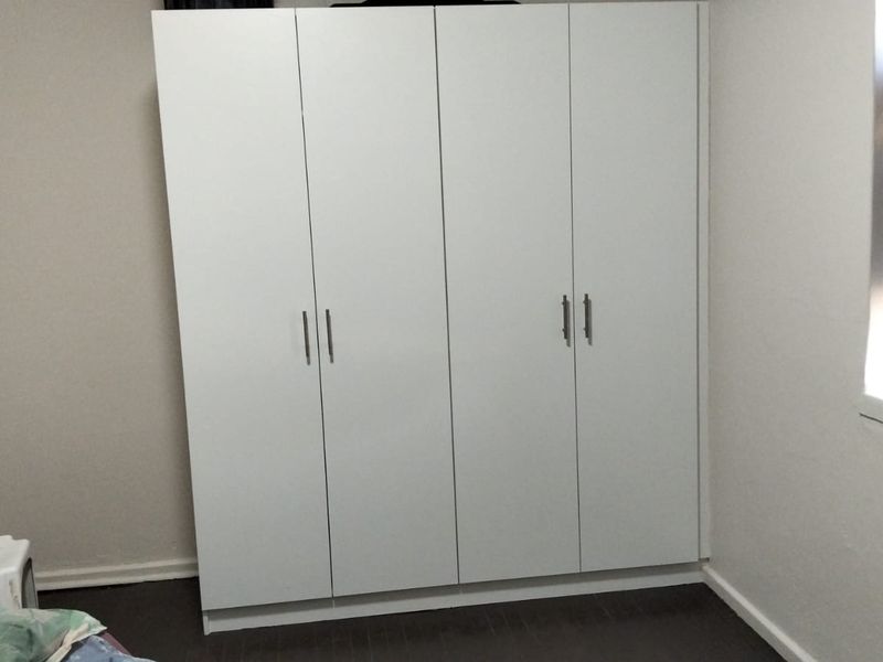 A bedroom featuring a clean, white built-in wardrobe with modern handles, providing ample storage space.