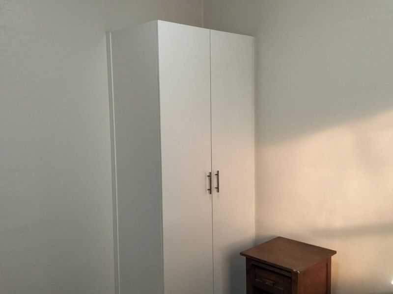 A simple bedroom interior featuring a clean white built-in wardrobe with modern handles.