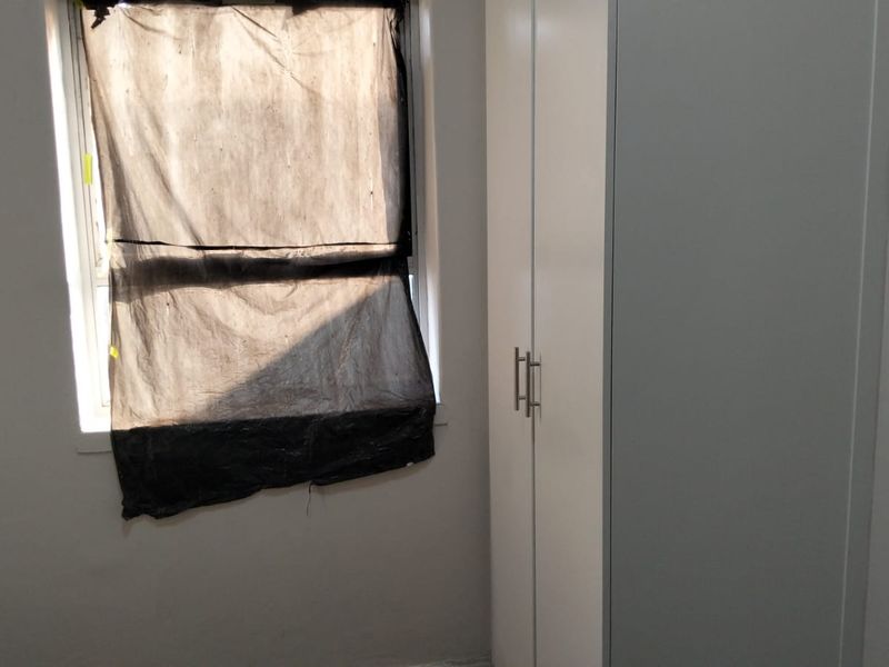 A simple bedroom featuring a built-in wardrobe and a window with a temporary plastic covering.