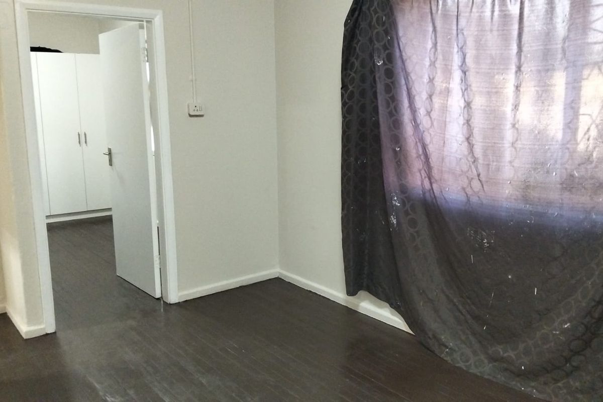 A vacant bedroom featuring dark laminate flooring, neutral walls, and built-in cupboards, offering a clean and versatile space ready for personalization.