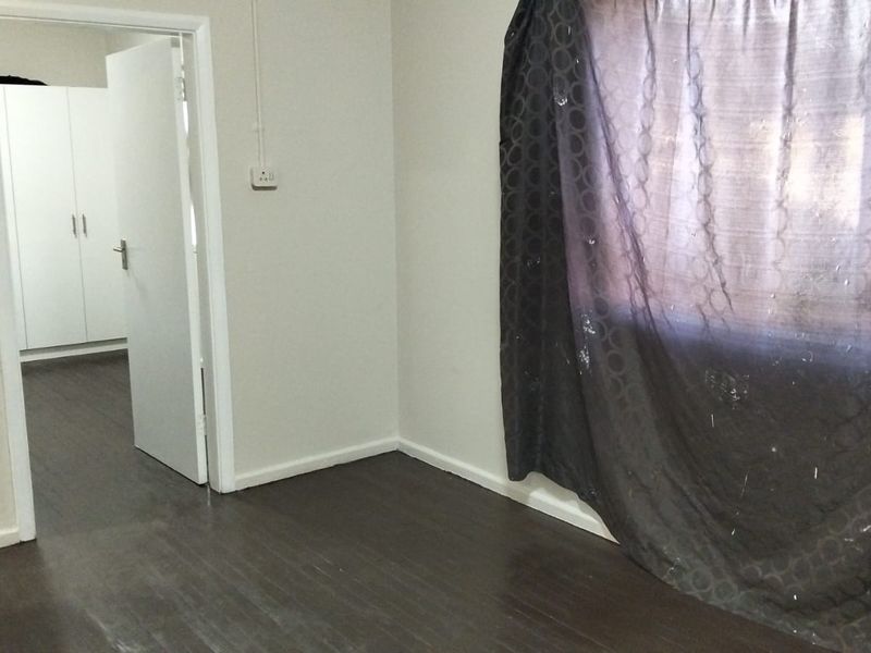 A vacant bedroom featuring dark laminate flooring, neutral walls, and built-in cupboards, offering a clean and versatile space ready for personalization.