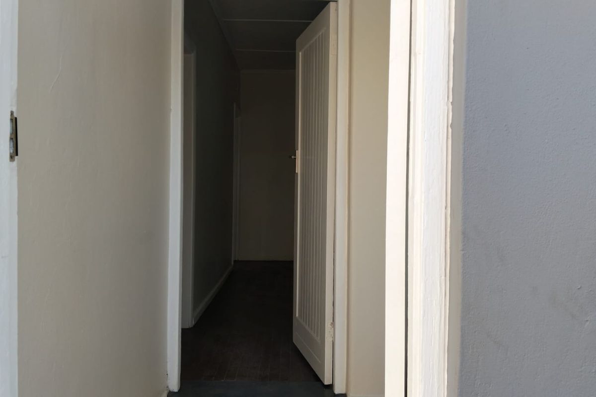 A view through an open doorway into a dark interior hallway with neutral wall finishes.