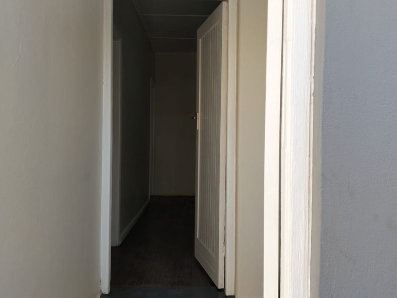 A view through an open doorway into a dark interior hallway with neutral wall finishes.