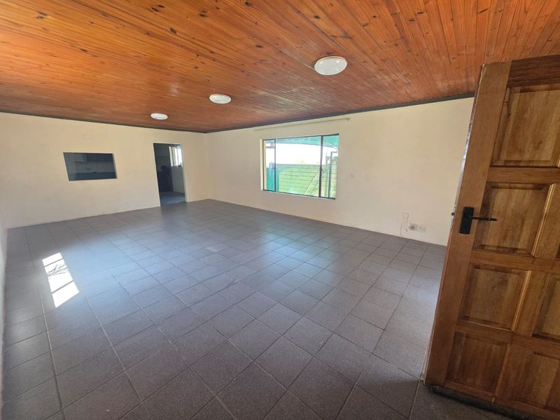 Spacious, empty living area featuring tiled flooring and a distinctive wooden tongue and groove ceiling, offering a blank canvas for interior design.