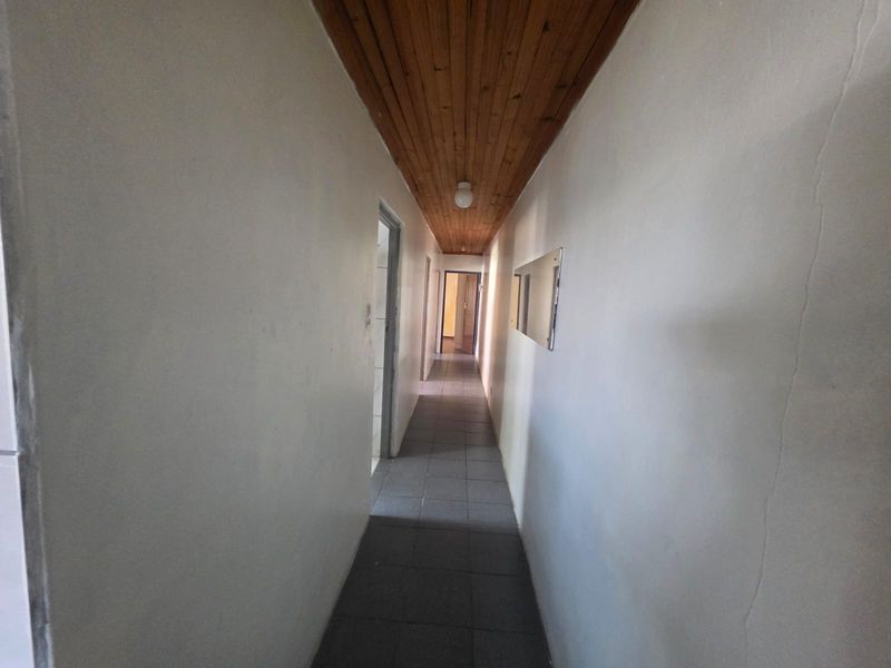 A narrow hallway featuring tiled flooring and a timber tongue and groove ceiling, showing signs of wear on the wall surfaces.