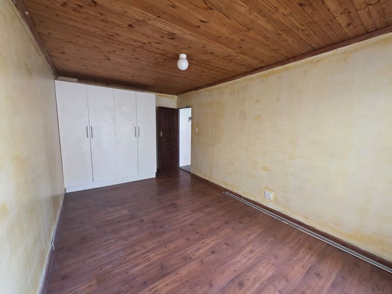 An empty bedroom featuring laminate flooring, a timber-clad ceiling, and built-in white cupboards, requiring cosmetic updates to the wall finishes.