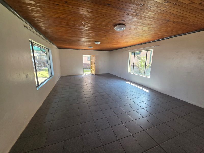 A spacious, empty living area featuring dark ceramic floor tiles and a warm timber tongue and groove ceiling with natural light.