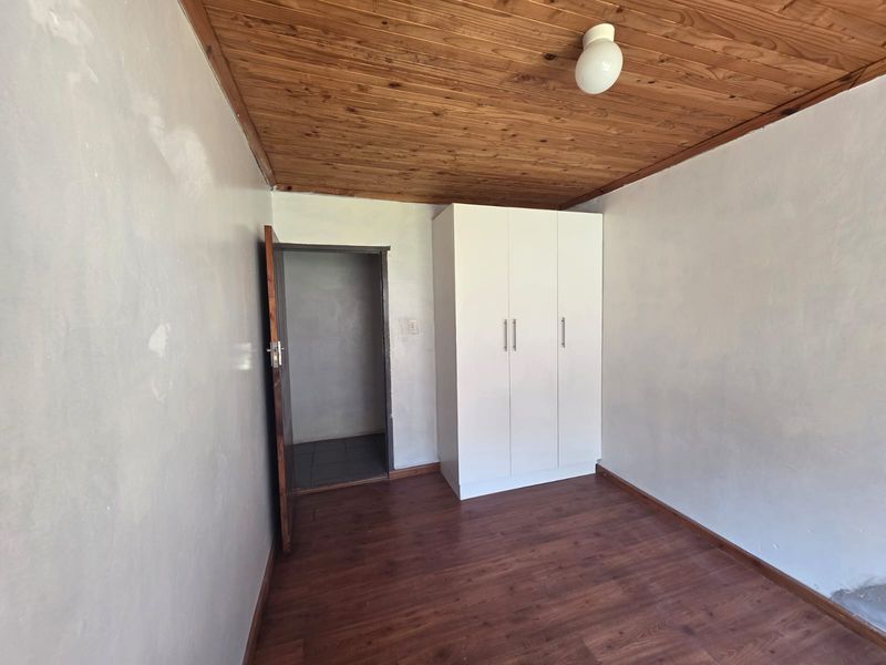 A bedroom featuring laminate flooring, a timber ceiling, and a built-in wardrobe, currently vacant and ready for renovation.