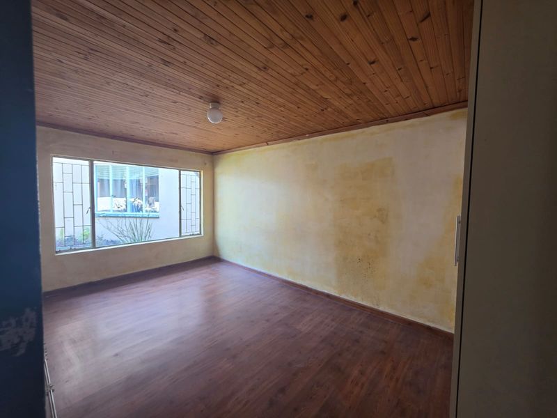 An empty bedroom featuring timber ceilings, laminate flooring, and built-in cupboards, requiring cosmetic updates to the wall finishes.