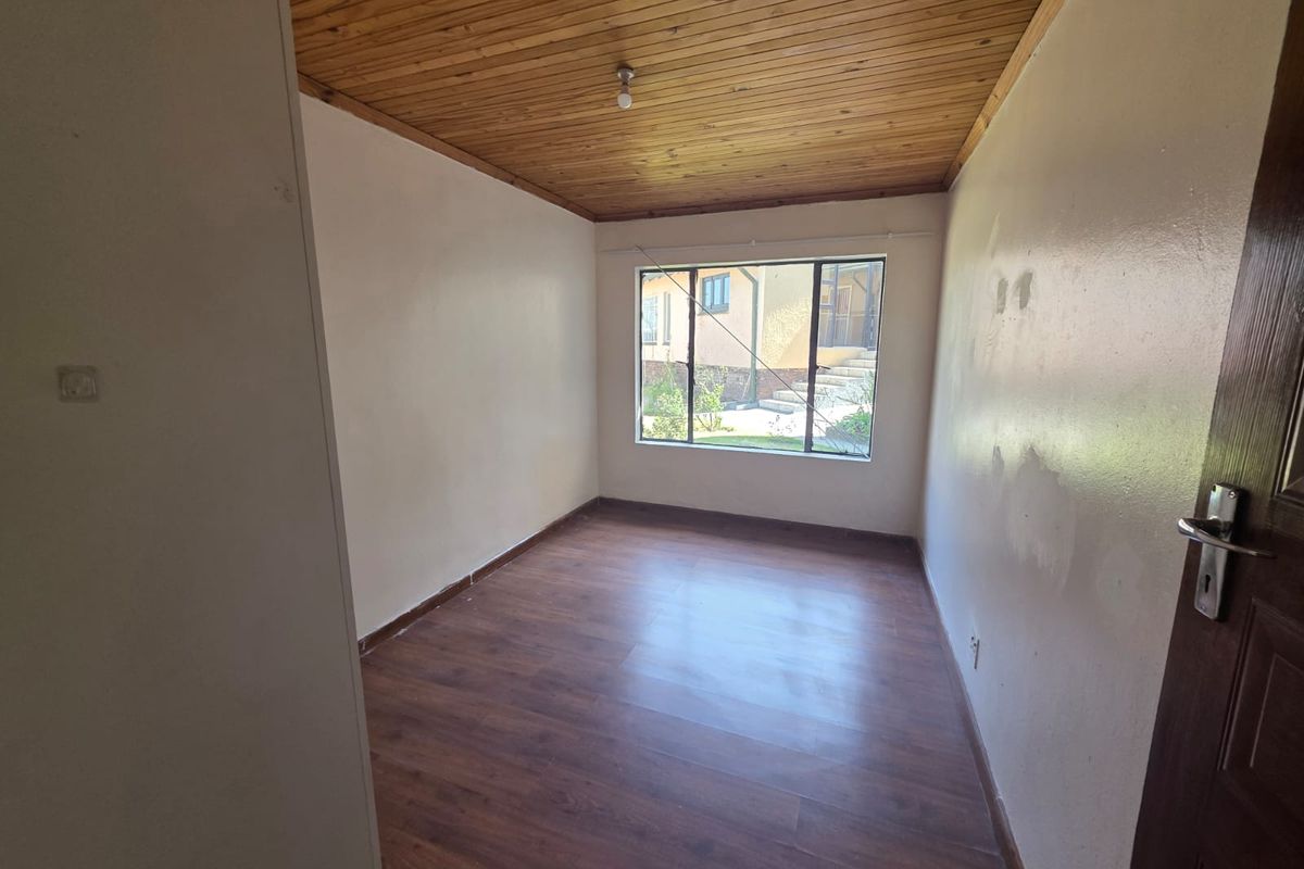 An empty bedroom featuring laminate flooring, a timber-clad ceiling, and an aluminium-framed window overlooking the exterior.