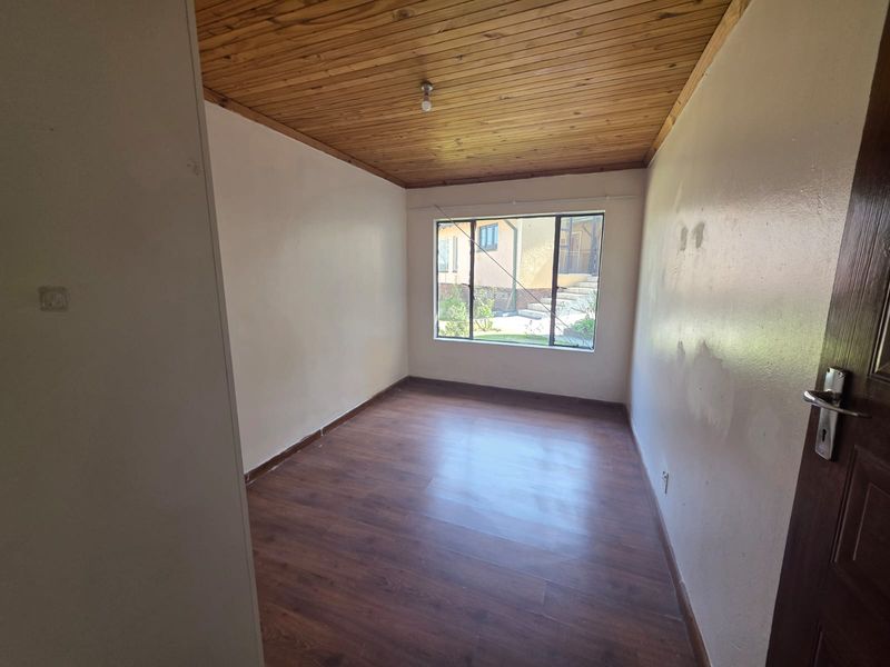 An empty bedroom featuring laminate flooring, a timber-clad ceiling, and an aluminium-framed window overlooking the exterior.