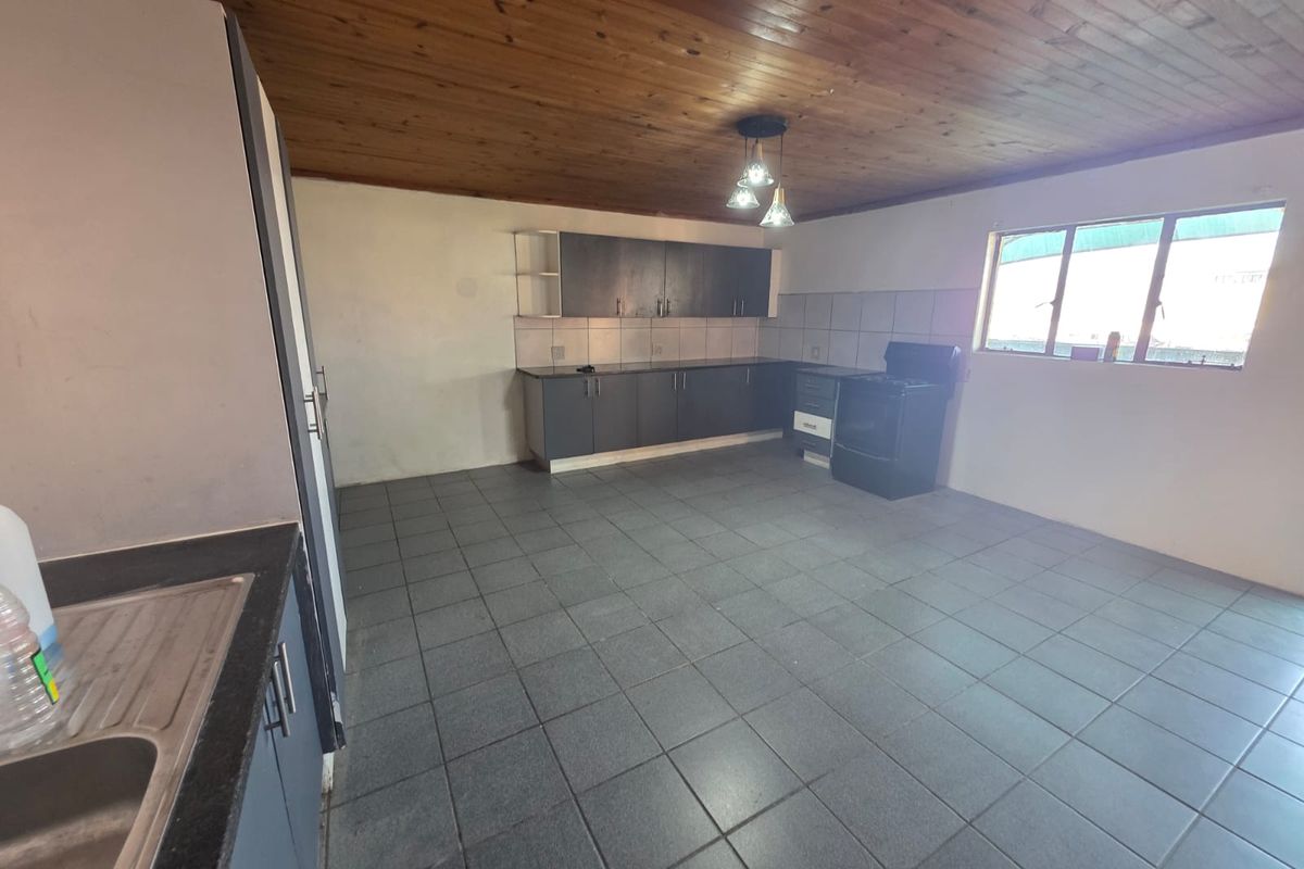Spacious kitchen featuring dark cabinetry, tiled flooring, a timber ceiling, and a freestanding stove, offering a functional layout with potential for modern updates.