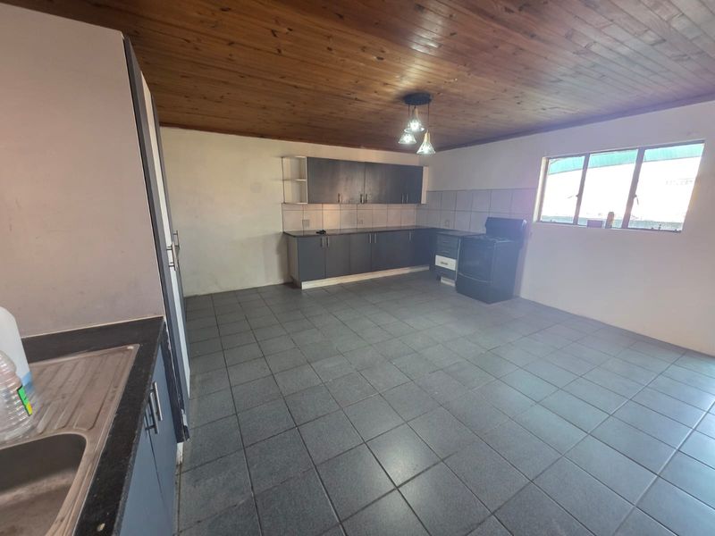 Spacious kitchen featuring dark cabinetry, tiled flooring, a timber ceiling, and a freestanding stove, offering a functional layout with potential for modern updates.